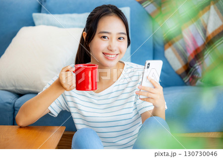 ソファーでくつろぎながらスマホを操作する女性 ソファーでくつろぎながらスマホを操作する女性 130730046