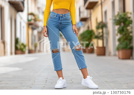 Young stylish woman wearing ripped jeans and white sneakers is standing in a city street Young stylish woman wearing ripped jeans and white sneakers is standing in a city street 130730176