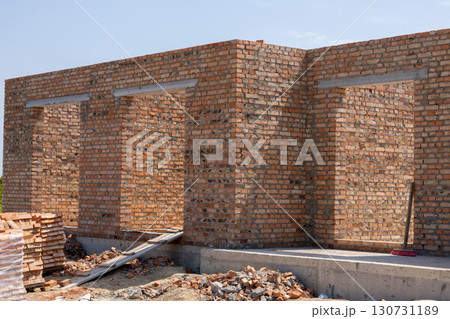 Unfinished red brick wall construction with concrete foundation and open doorways. New building masonry structure in progress on a sunny site. 130731189