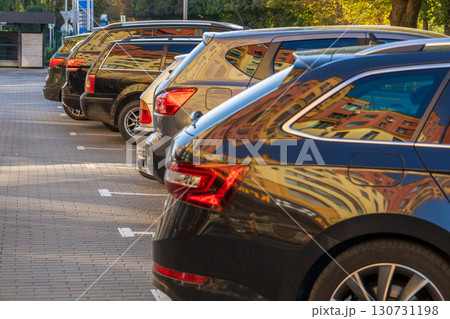 Modern cars parked in a row on a sunny urban parking lot. Bright building reflections on dark vehicle windows and shiny car bodies. Modern cars parked in a row on a sunny urban parking lot. Bright building reflections on dark vehicle windows and shiny car bodies. 130731198