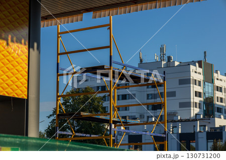 Tall yellow and blue scaffolding stands in front of modern city buildings. Clear blue sky above urban construction site scene. Building progress. Tall yellow and blue scaffolding stands in front of modern city buildings. Clear blue sky above urban construction site scene. Building progress. 130731200