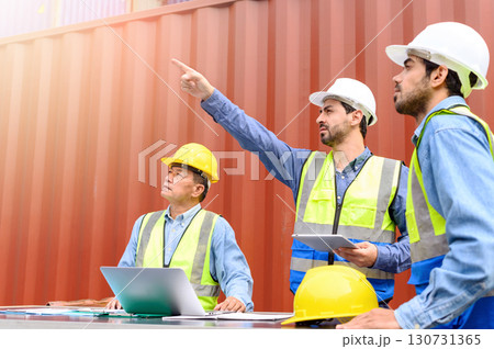 Supervisor holding tablet meeting with colleagues about logistics operations in Container terminal. Industrial Engineer in white hard hats and safety vests for safety. Supervisor holding tablet meeting with colleagues about logistics operations in Container terminal. Industrial Engineer in white hard hats and safety vests for safety. 130731365