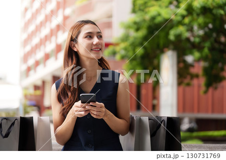 Urban Shopping. Woman smiling while using smartphone outdoors with shopping bags. Urban Shopping. Woman smiling while using smartphone outdoors with shopping bags. 130731769