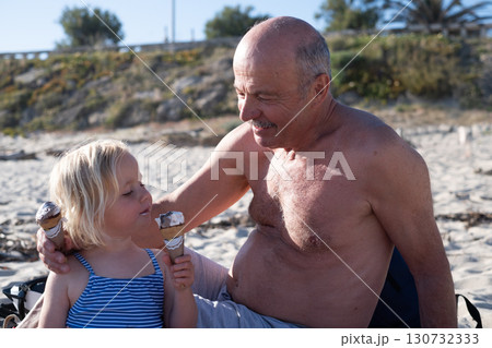 European girl eating ice cream on the beach with her grandfather 130732333