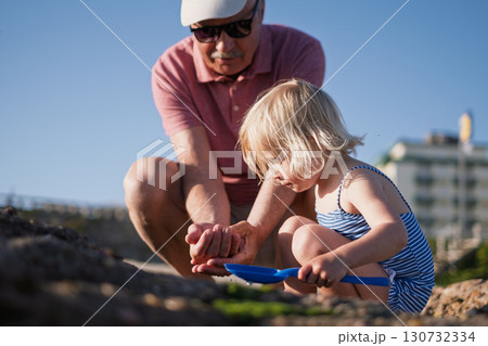 girl playing with grandfather in sand on the beach during summer holidays girl playing with grandfather in sand on the beach during summer holidays 130732334