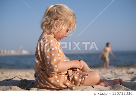 blonde girl sitting on the beach and playing alone 130732336
