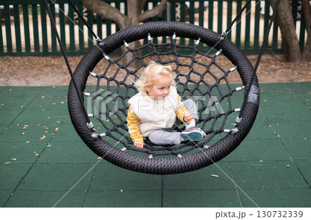 little European girl swinging on a swing at the playground 130732339