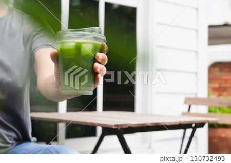 Woman reaching hand with glass of iced Matcha green tea to camera. Woman reaching hand with glass of iced Matcha green tea to camera. 130732493