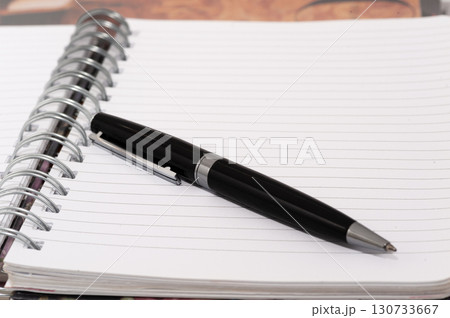 A black pen is on a white page of a spiral bound notebook A black pen is on a white page of a spiral bound notebook 130733667