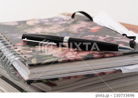 A black pen is on top of a spiral bound notebook 130733696
