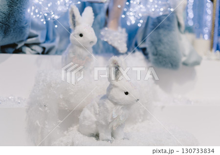 Two white rabbits are sitting on a snow pile 130733834