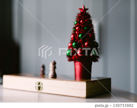 A red and green Christmas tree sits on a table next to a chess set 130733882