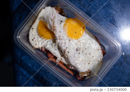 Simple meal of two fried eggs placed over grilled sausage, served in a clear plastic container. Simple meal of two fried eggs placed over grilled sausage, served in a clear plastic container. 130734000