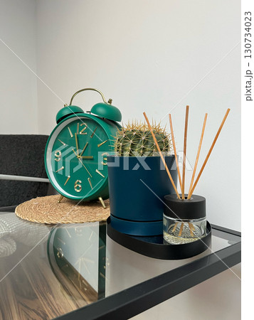 A green alarm clock sits on a table next to a small plant A green alarm clock sits on a table next to a small plant 130734023