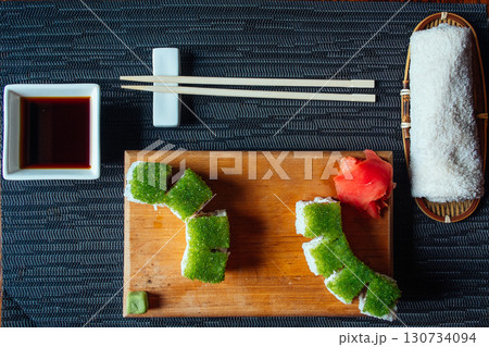 A plate of sushi with green seaweed and a small bowl of sauce 130734094