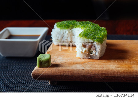 A sushi roll with seaweed on top sits on a wooden cutting board 130734114