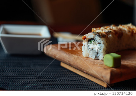 A sushi roll sits on a wooden cutting board with a small green leaf on top A sushi roll sits on a wooden cutting board with a small green leaf on top 130734120