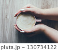 A hand holding a cup of coffee on a wooden table 130734122