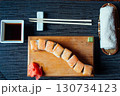 A sushi roll sits on a wooden cutting board with chopsticks and a napkin nearby 130734123