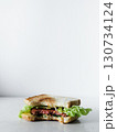 A sandwich with lettuce and meat is cut in half and placed on a white background 130734124