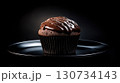Chocolate cupcake with chocolate frosting sits on a black plate 130734143