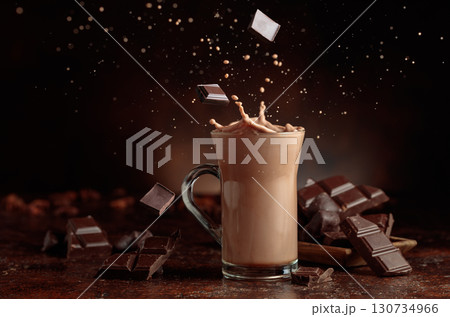 Pieces of bitter chocolate fall in glass mug with cocoa drink. 130734966