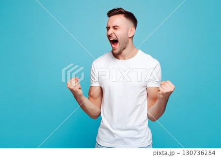 Excited young man shows pure emotion, shouting with closed eyes and tightly clenched fists, celebrating a big success. 130736284