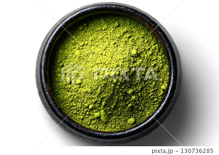 Fine bright vibrant green matcha tea powder fills a simple rustic dark ceramic bowl, naturally appearing from an overhead view. 130736285