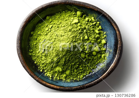Bright green matcha powder rests in a dark blue ceramic bowl. This fine tea powder forms a soft pile inside the round container. 130736286