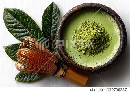 Fresh green matcha tea powder sits in a traditional bowl with a bamboo whisk and natural leaves. 130736287