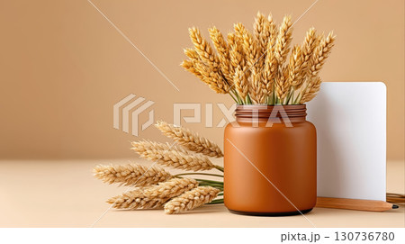 Golden wheat stalks in brown jar with pencil and white board on beige background, warm and cozy autumn decor 130736780