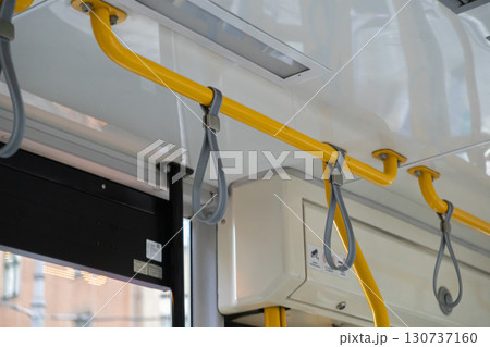 Bright yellow grab bars and grey strap handles provide essential stability for passengers within modern public transport, symbolizing urban mobility and safe daily commute 130737160
