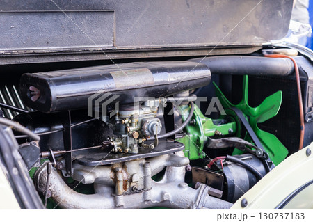 Close-up of a classic car engine showing carburetor, air filter, and vibrant green cooling fan, representing vintage mechanical engineering and automotive restoration Close-up of a classic car engine showing carburetor, air filter, and vibrant green cooling fan, representing vintage mechanical engineering and automotive restoration 130737183