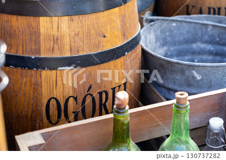 Close-up of a rustic wooden barrel with OGORKI text, vintage green bottles, and metal bucket, reflecting traditional food market culture 130737282