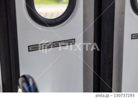 White public transport door with round window and safety warning sign, ATTENTION THEY OPEN INWARDS, guiding passengers for safe urban transit and commuter awareness White public transport door with round window and safety warning sign, ATTENTION THEY OPEN INWARDS, guiding passengers for safe urban transit and commuter awareness 130737293