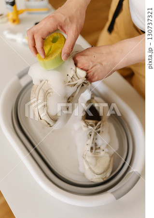 Top view of man washing dirty white sneakers using sponge and soap in basin at home, focusing on removing stains and keeping footwear clean and fresh, close-up. Concept of footwear maintenance. 130737321