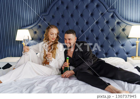 A man and a woman in silk pajamas with champagne are lying on a bed. A man and a woman in silk pajamas with champagne are lying on a bed. 130737945