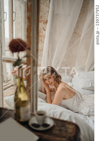 a young blonde woman in a white dress on white sheets by the window a young blonde woman in a white dress on white sheets by the window 130737952