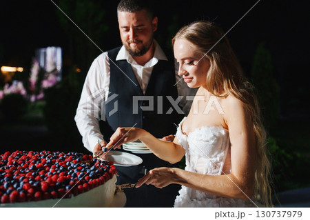Bride and groom cut a large round cake decorated with berries in the night. Bride and groom cut a large round cake decorated with berries in the night. 130737979