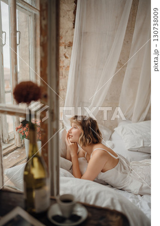 a young blonde woman in a white dress on white sheets by the window a young blonde woman in a white dress on white sheets by the window 130738009