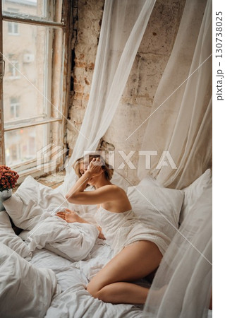 an attractive blonde woman in a white dress on white sheets 130738025