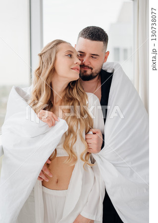 A gentle and romantic man and woman wrapped in a blanket on the windowsill A gentle and romantic man and woman wrapped in a blanket on the windowsill 130738077
