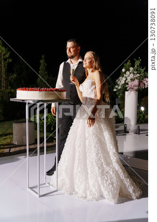 Bride and groom with a large round cake decorated with berries in the night. 130738091
