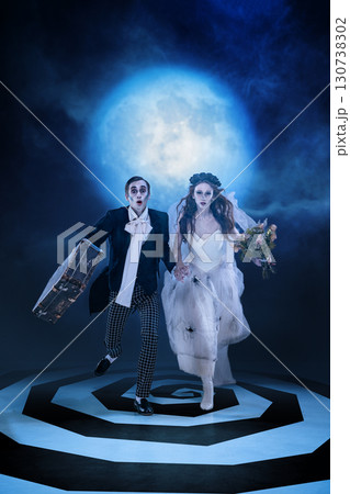 Zombie wedding couple running with suitcase and flowers under full moon Zombie wedding couple running with suitcase and flowers under full moon 130738302