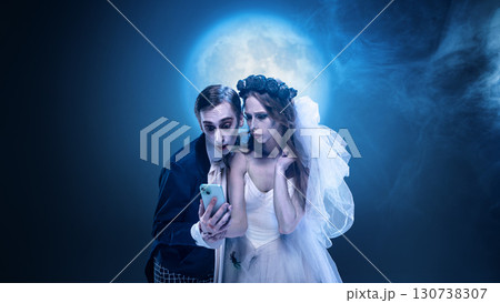 Surreal gothic wedding couple looking at smartphone under full moon Surreal gothic wedding couple looking at smartphone under full moon 130738307