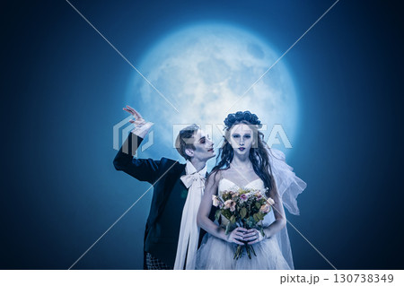 Gothic bride and groom posing with bouquet under full moonlight in eerie wedding fashion Gothic bride and groom posing with bouquet under full moonlight in eerie wedding fashion 130738349
