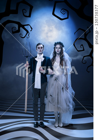 Gothic couple in eerie wedding costume standing under moonlight with dramatic expression 130738377