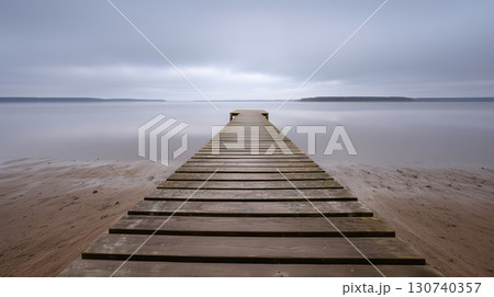 Wooden pier stretching into calm lake under cloudy sky Wooden pier stretching into calm lake under cloudy sky 130740357