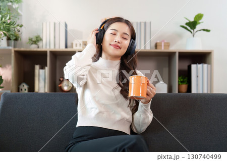 Music and Relaxation. Young woman enjoying music with headphones and coffee at home. Music and Relaxation. Young woman enjoying music with headphones and coffee at home. 130740499