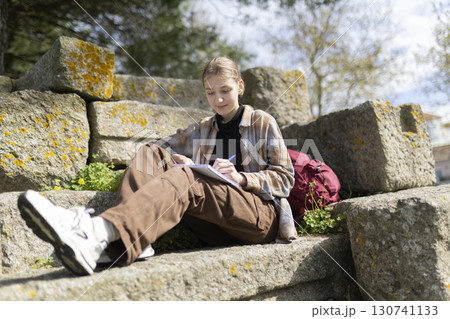 Young archaeologist writing notes outdoors on ancient ruins Young archaeologist writing notes outdoors on ancient ruins 130741133